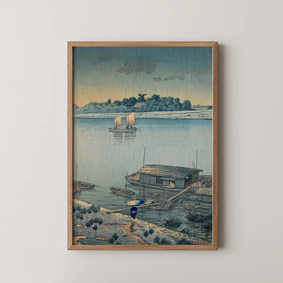 Framed painting of a serene riverside scene depicting boats on water, a small house, and a figure walking with an umbrella under a cloudy sky.