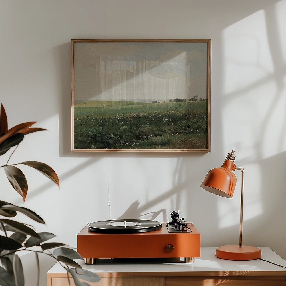 A vintage landscape painting framed and displayed above an orange record player and a matching orange desk lamp in a sunlit room.