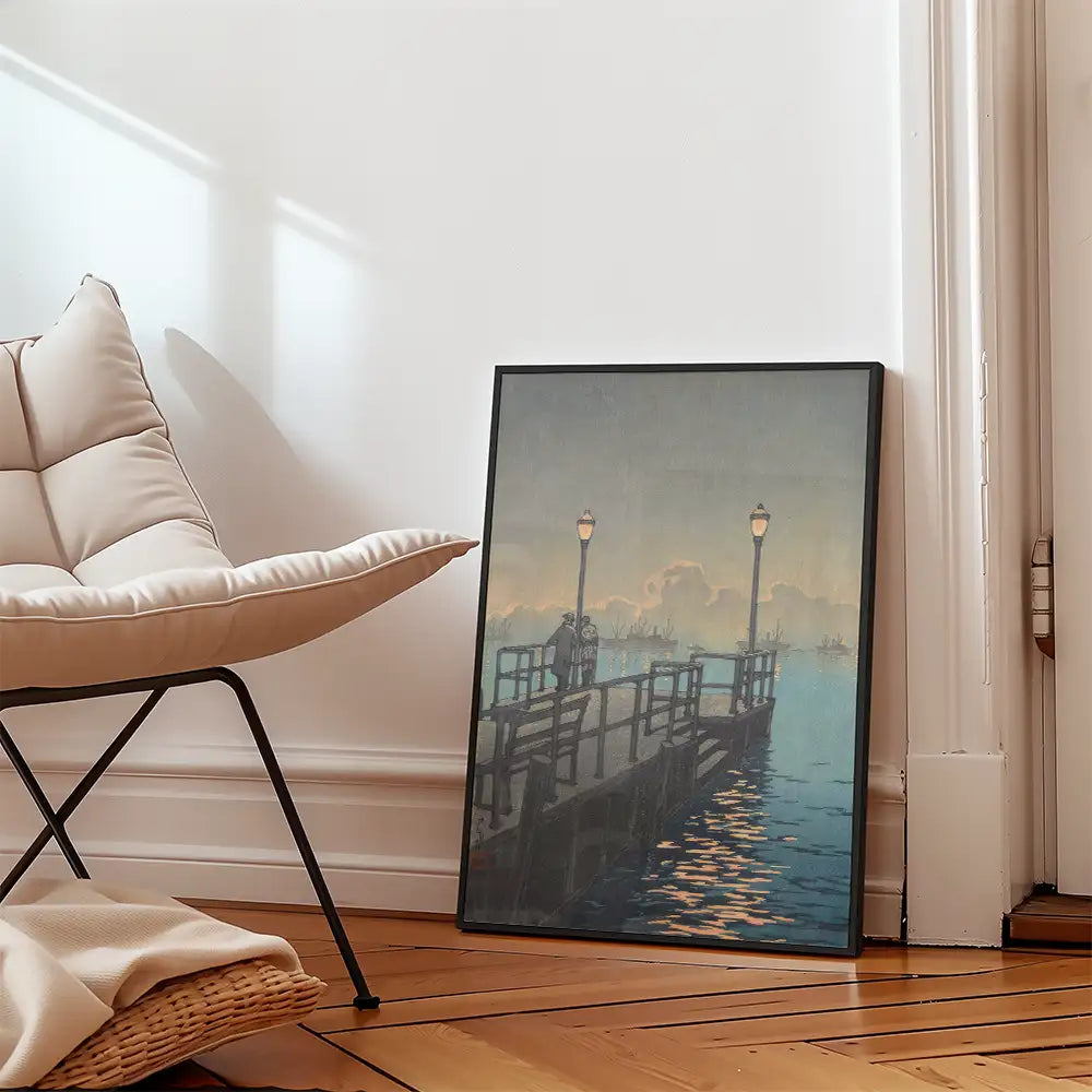 Framed painting of a pier at dusk with street lamps, positioned next to a modern chair in a cozy interior setting.