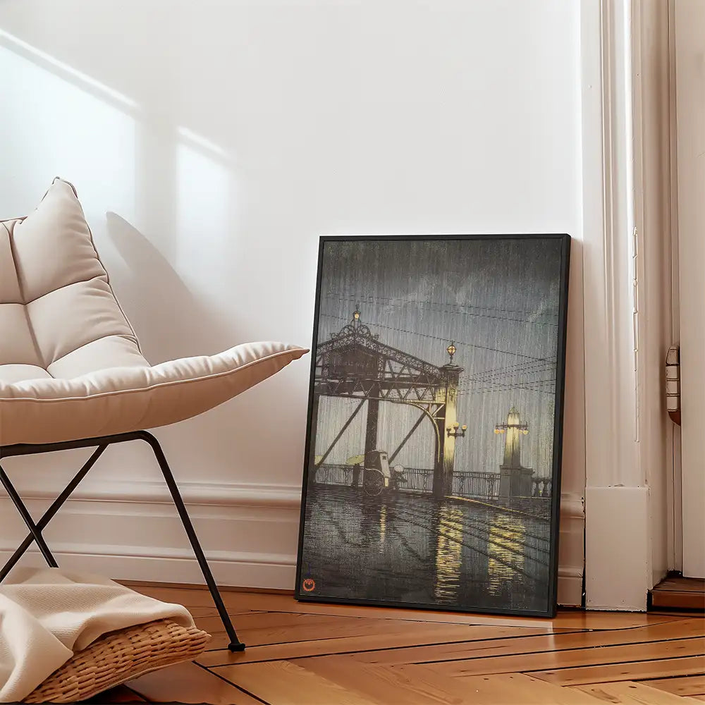 Framed painting of a bridge at night with reflections on water, placed next to a modern chair in a minimalist room.