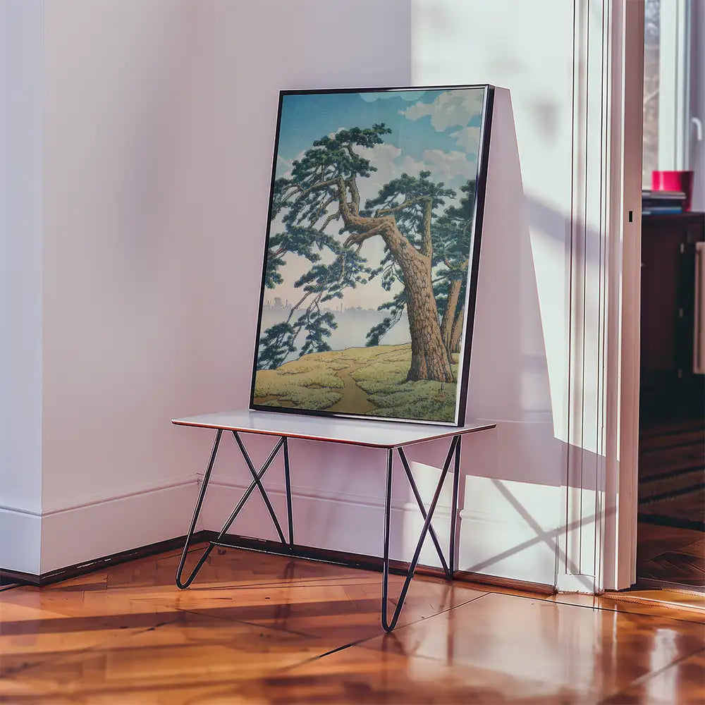 Painting of a tree against a blue sky displayed on a modern table in a bright room.