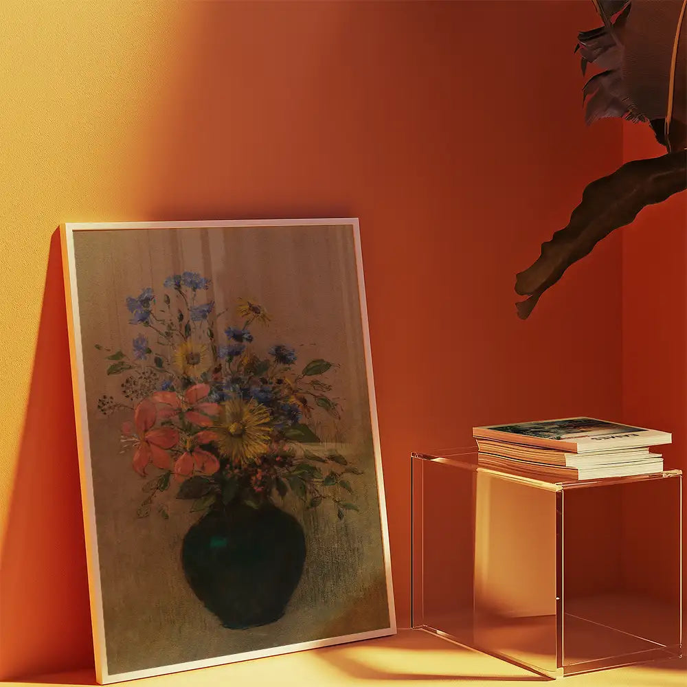 Floral painting in a black vase leaning against an orange wall, with stacked books on a transparent acrylic table.