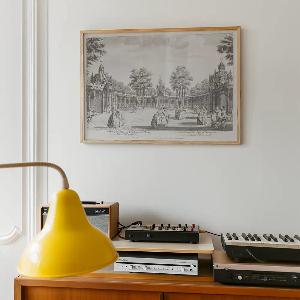 Framed black and white historical painting depicting a garden scene, displayed on a wall above a wooden sideboard with audio equipment and a yellow lamp in the foreground.