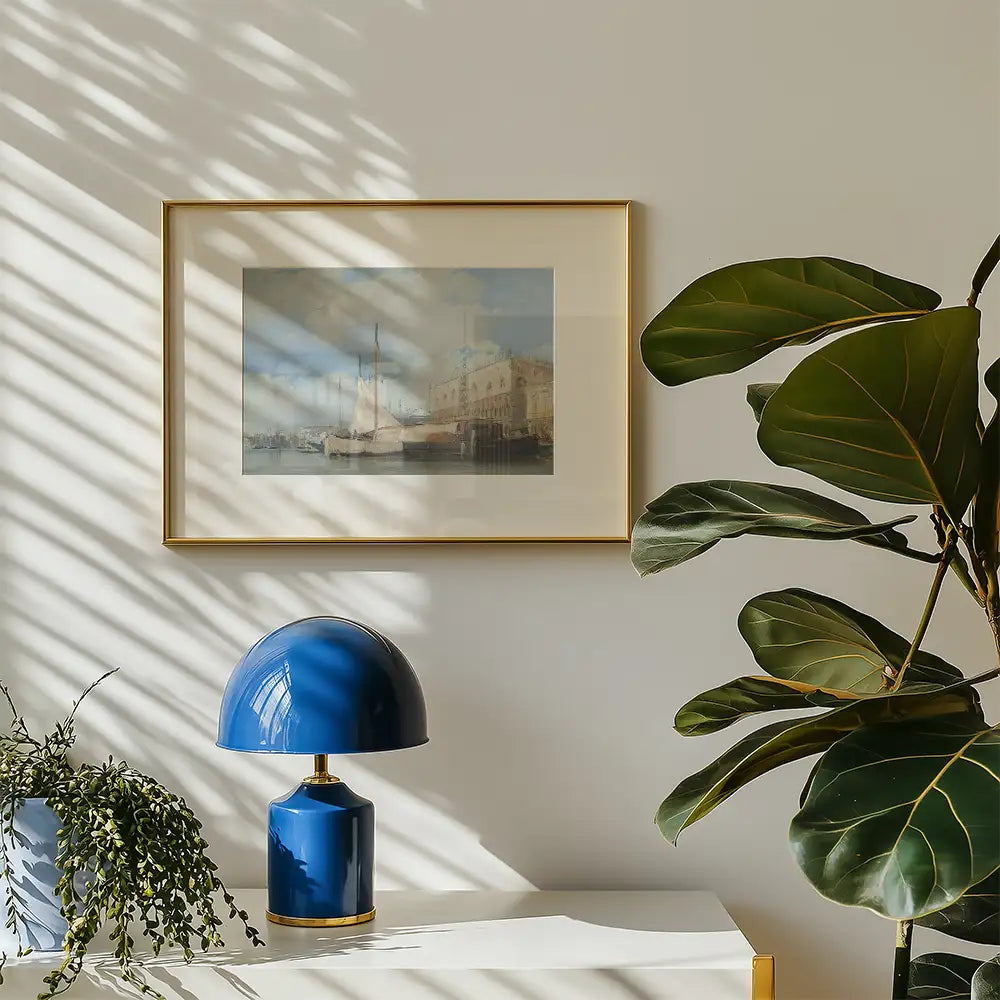 Framed painting of a serene waterfront scene with a sailboat and historic buildings, displayed on a wall beside a stylish blue lamp and a green plant.