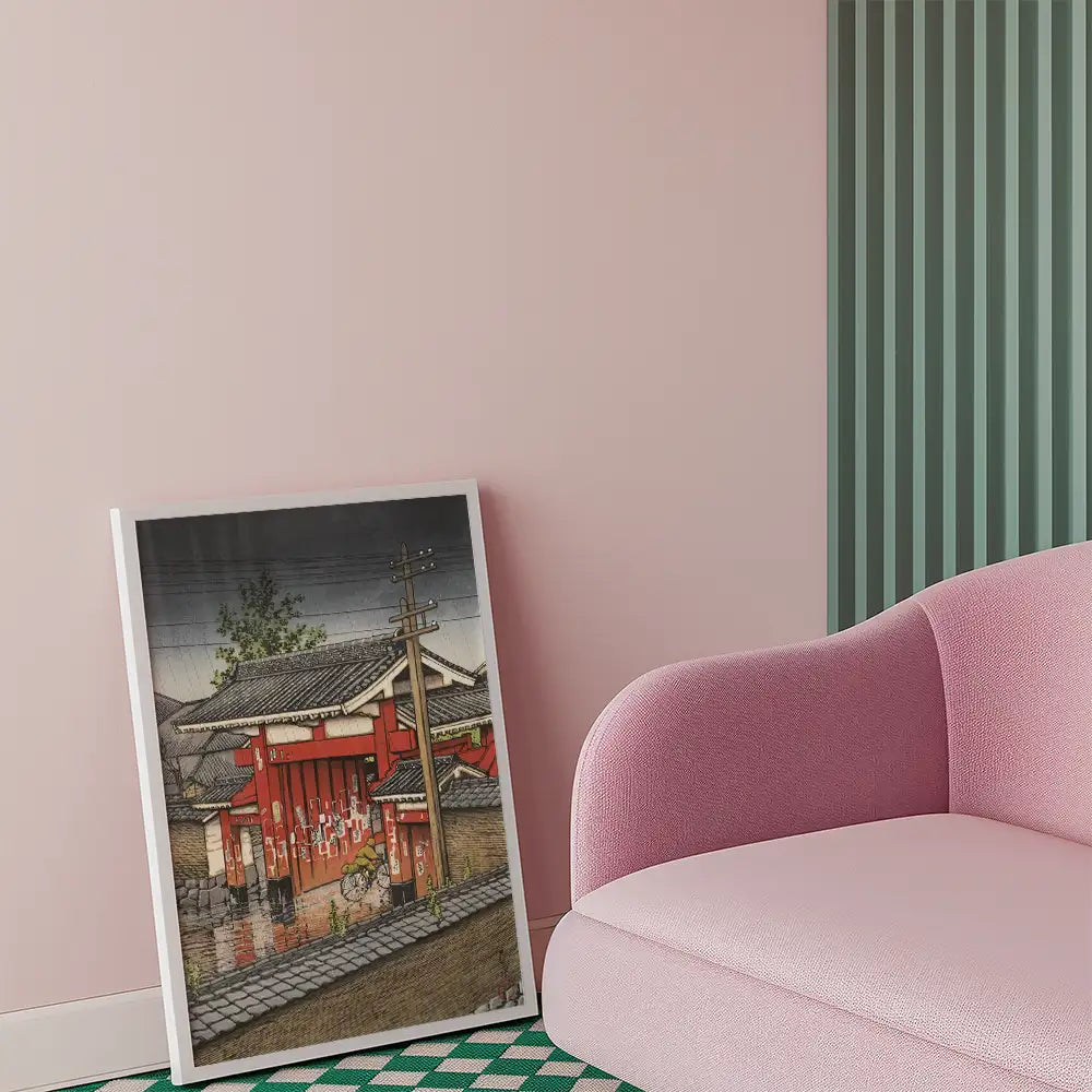 Painting of a traditional Japanese building in a framed display next to a pink sofa in a modern interior setting.