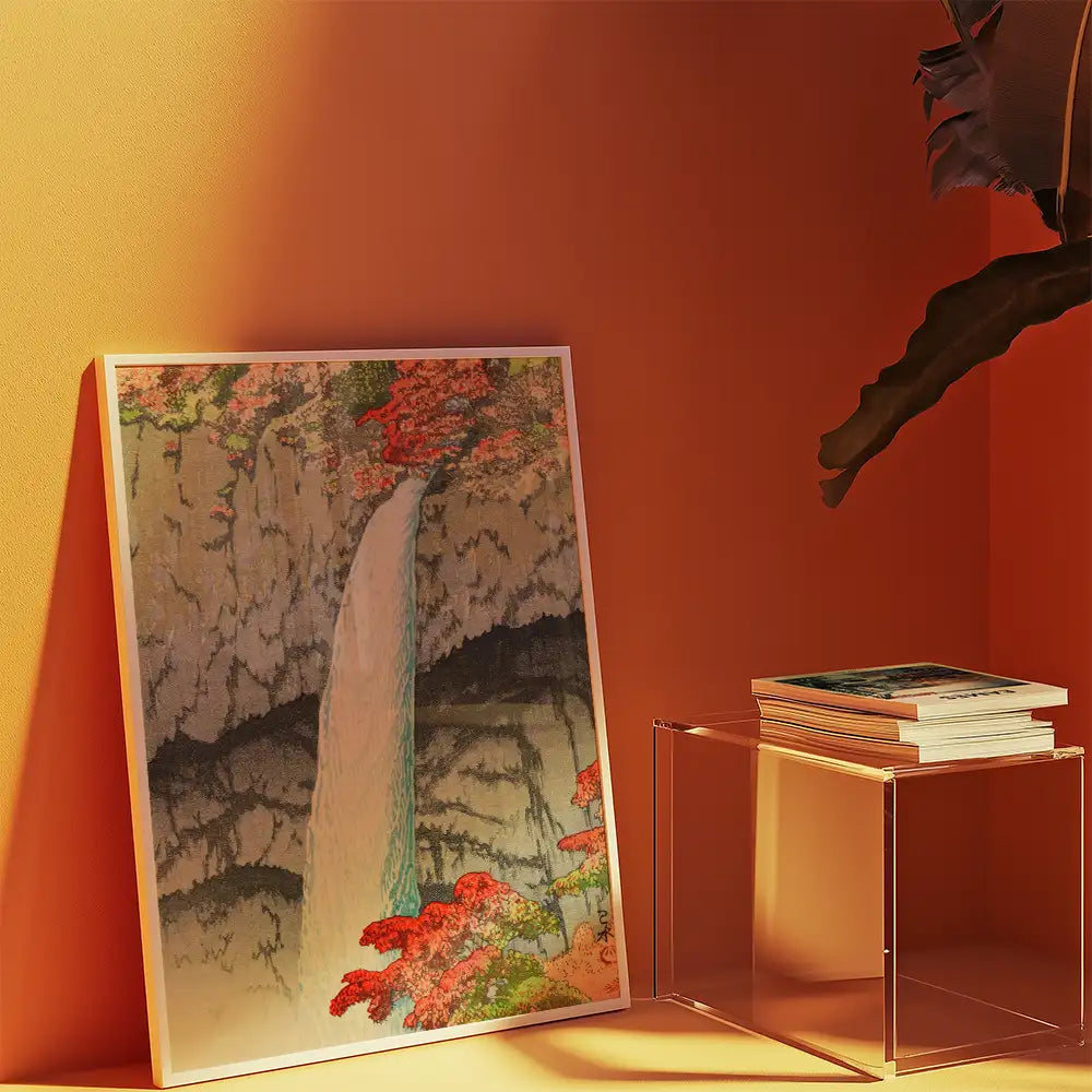 Artistic painting of a waterfall surrounded by vibrant flowers, displayed against an orange wall next to a small table with stacked books.
