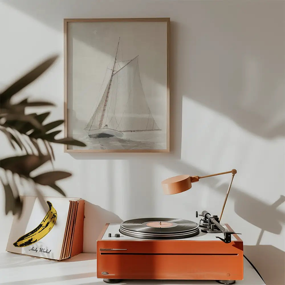 Painting of a sailing boat in a light wooden frame, displayed above a modern record player with a decorative banana artwork nearby.