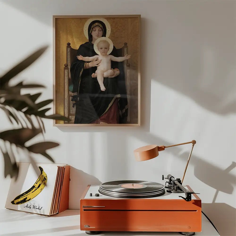 Framed painting of a Madonna and child hanging on a wall above a vintage turntable with an orange finish and a warm desk lamp.