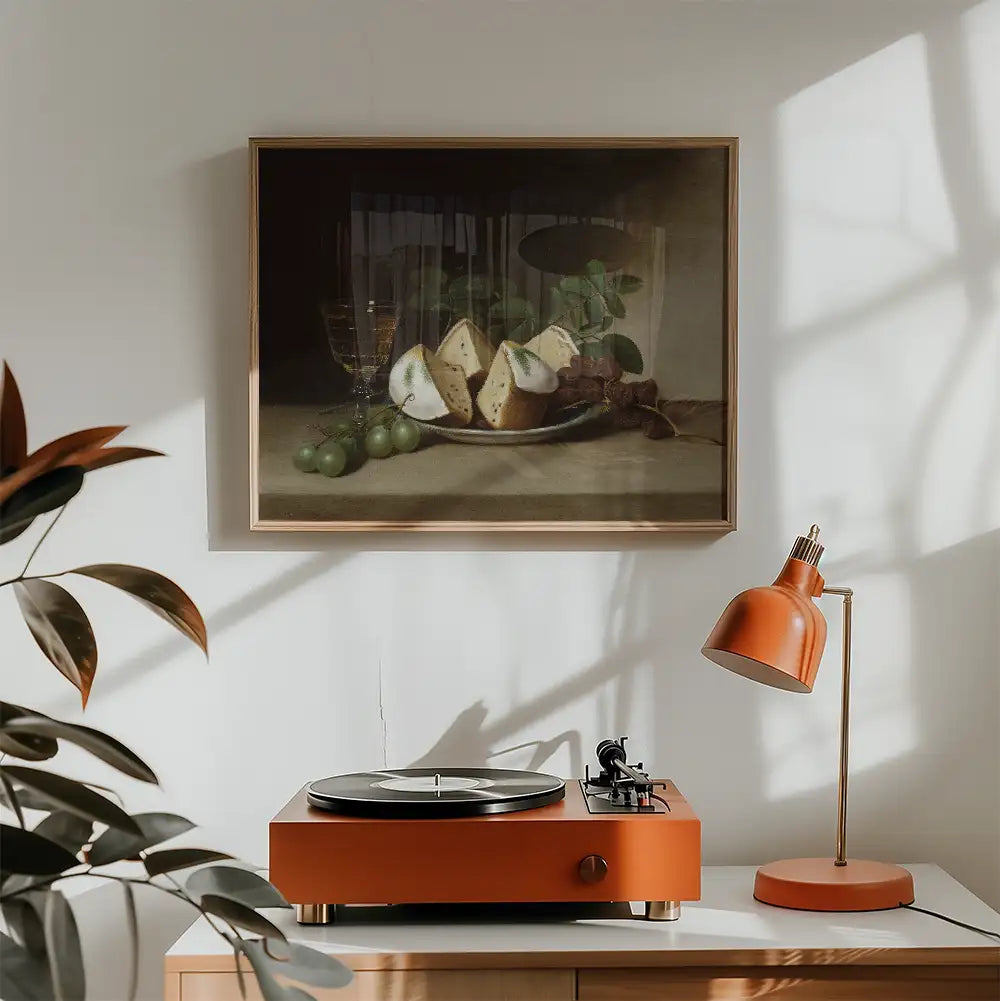 Painting of a still life featuring a platter of cheese, grapes, and glasses, framed and hung above an orange turntable and lamp in a stylish interior setting with natural light.