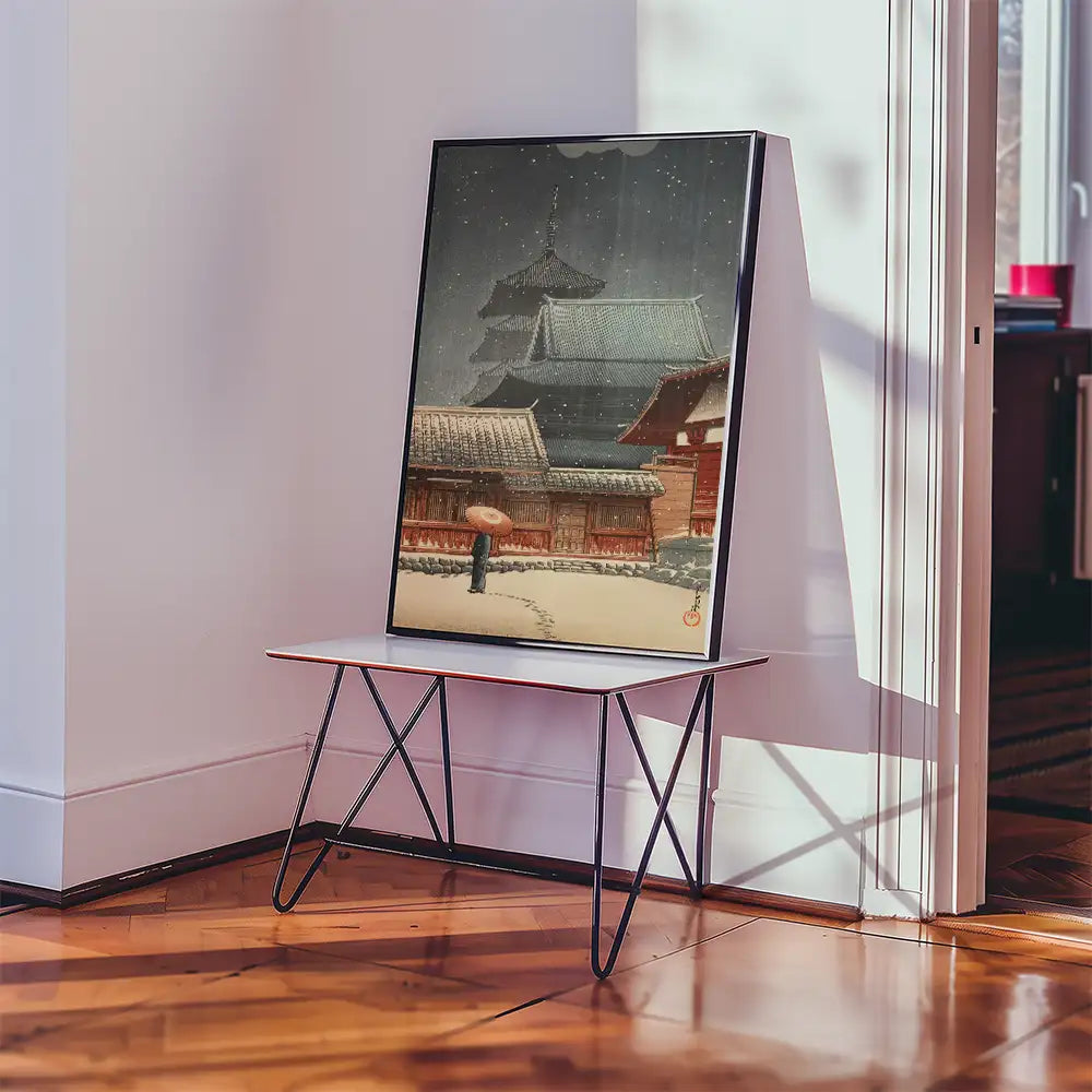 Painting of a snowy scene featuring traditional Japanese architecture, displayed on a minimalist metal table in a well-lit room.
