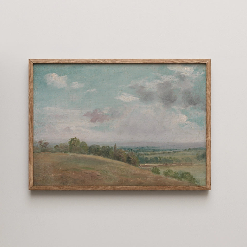 Landscape painting with soft blue skies and rolling hills framed in natural wood.