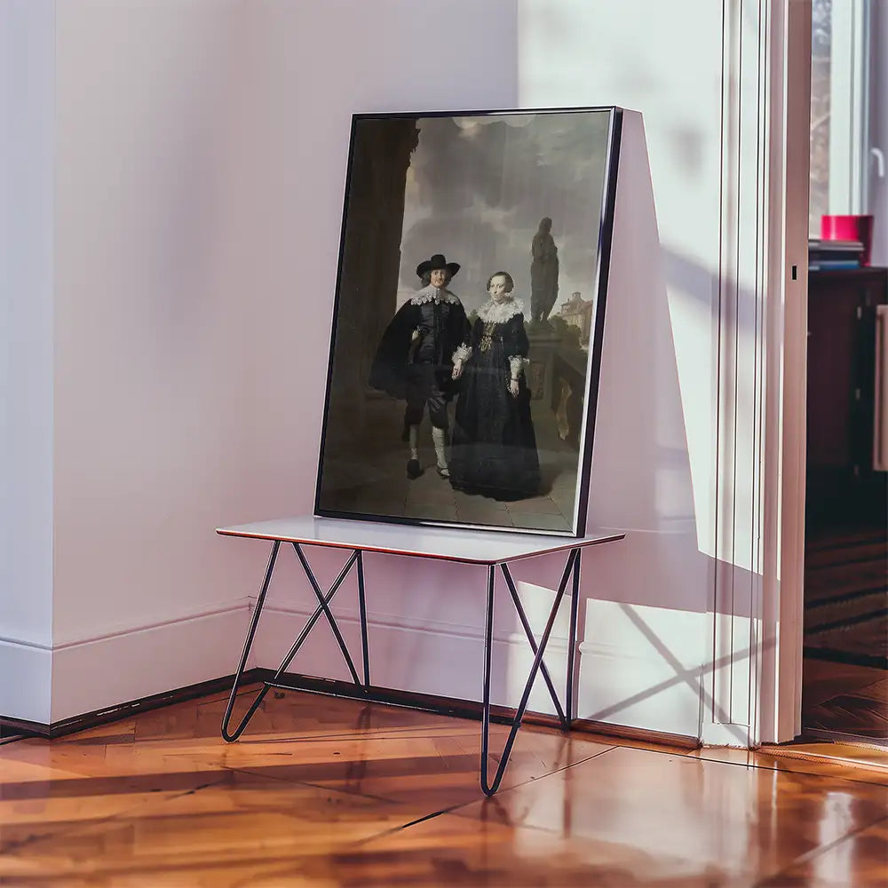 Framed painting of a man and woman in historical attire displayed on a modern table in a bright room with wooden flooring.
