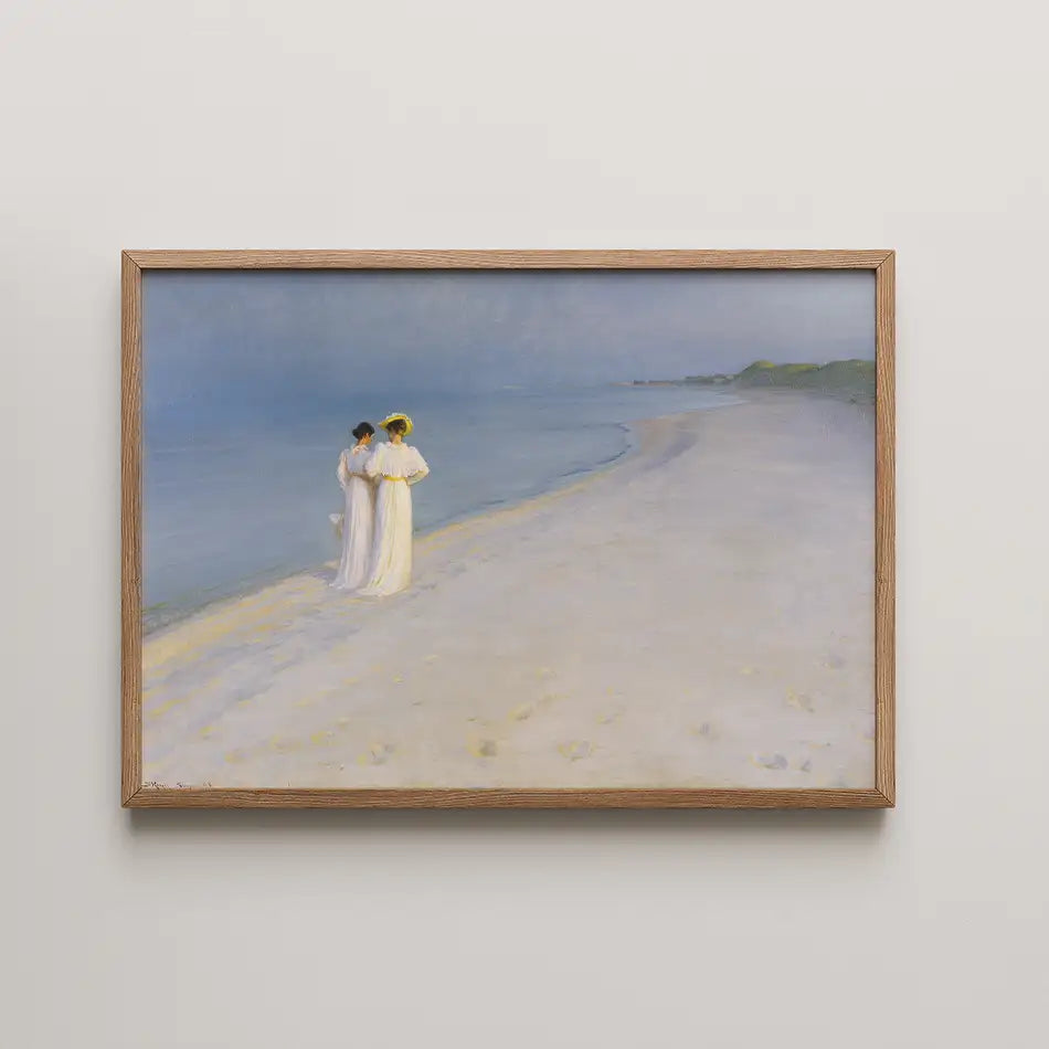 A tranquil beach scene painting featuring two women in white dresses standing on the shore, framed in a light wooden frame.
