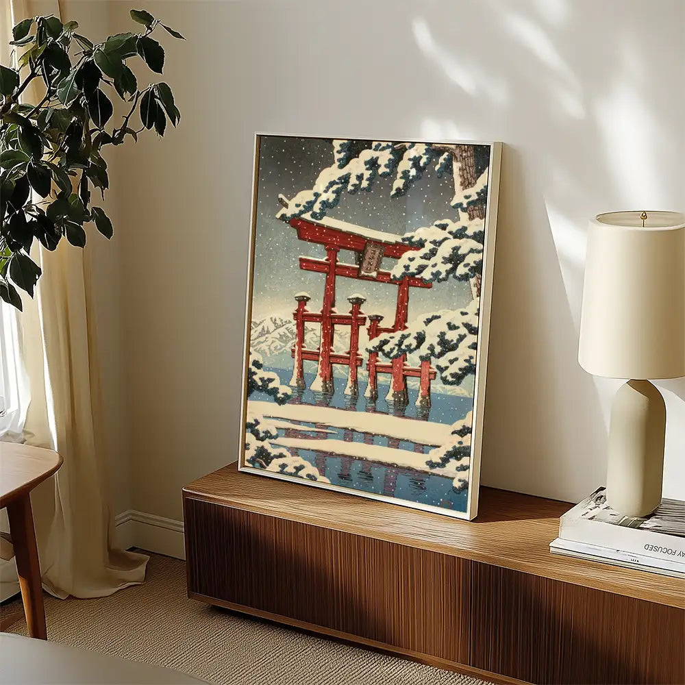 Framed painting of a red torii gate surrounded by snow-covered trees and mountains, displayed in a modern interior setting.